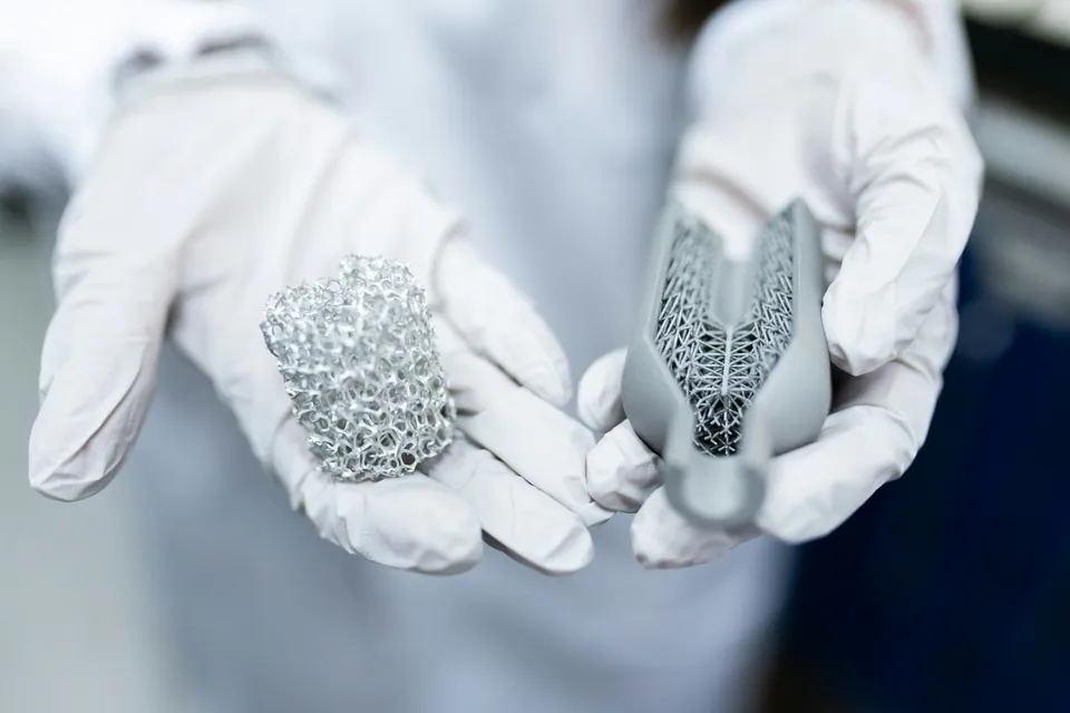 Gloved hands holding 3D-printed metal lattice parts