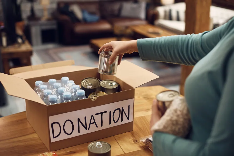 Person packing canned food and water into a donation box