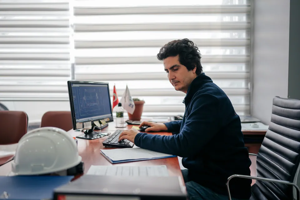 Engineer working at a desktop computer next to a hard hat