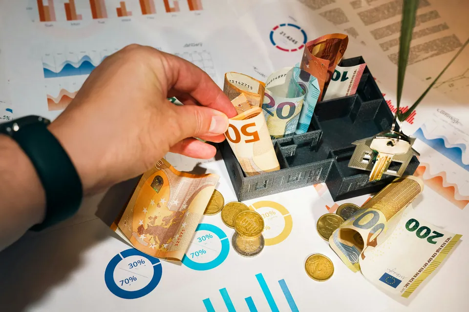 Hand placing euro banknotes into a small model house over printed charts