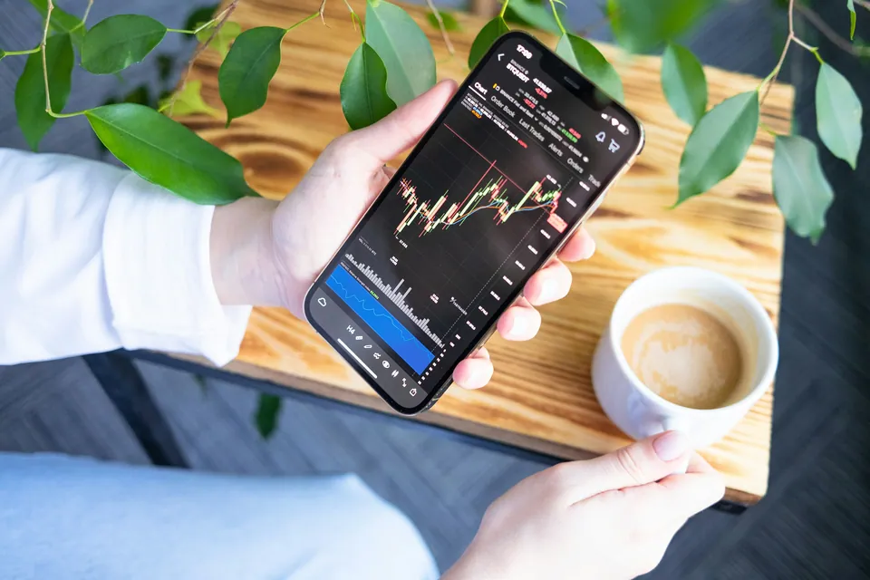 Hand holding a phone with a candlestick chart beside a latte
