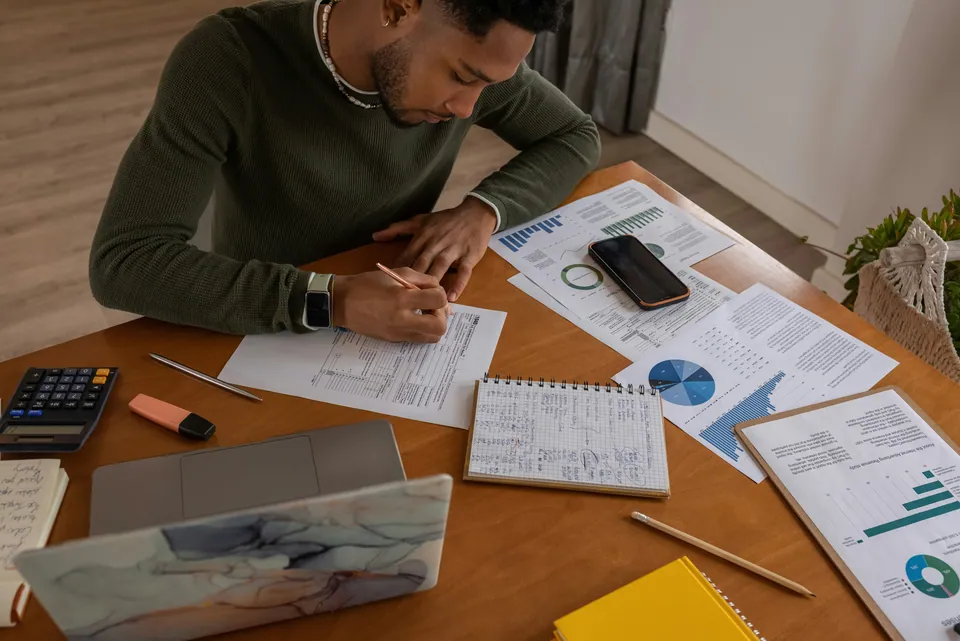 Man working through printed charts with a calculator at a wooden table