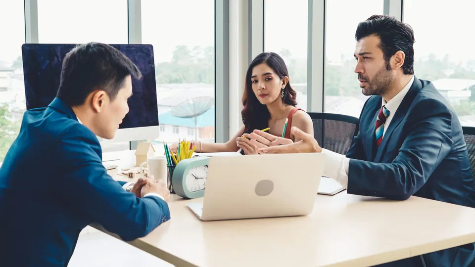 Advisor meeting a couple across a desk with a laptop