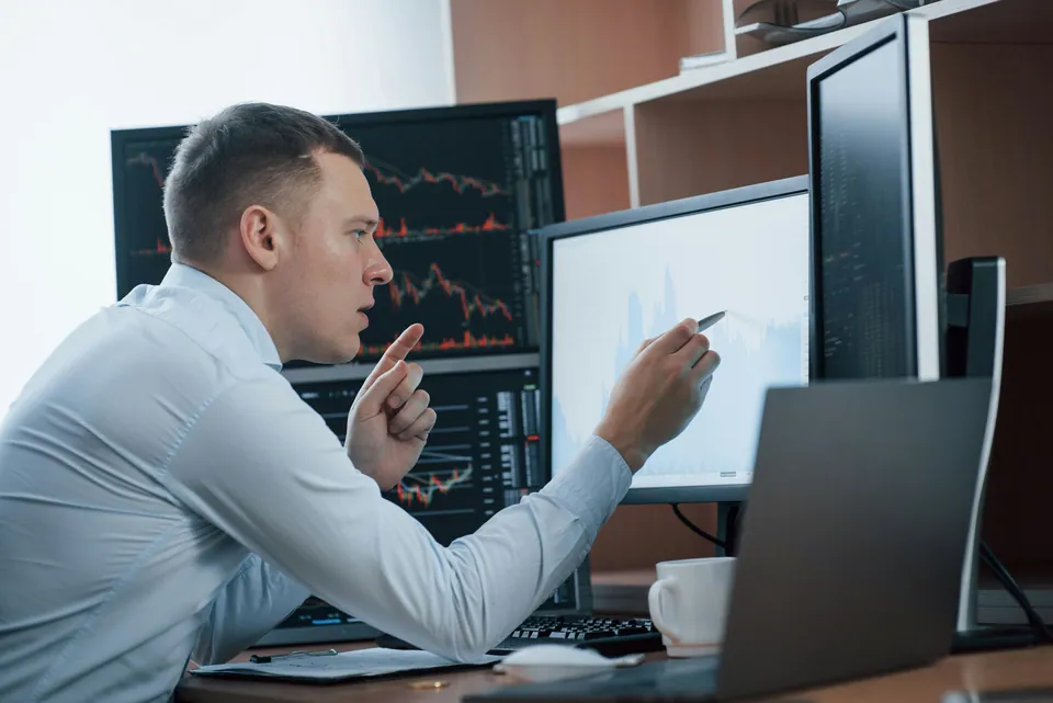 Analyst gesturing at chart monitors while explaining a point
