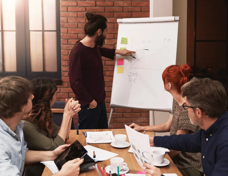 Man presenting at a flip chart to colleagues around a table
