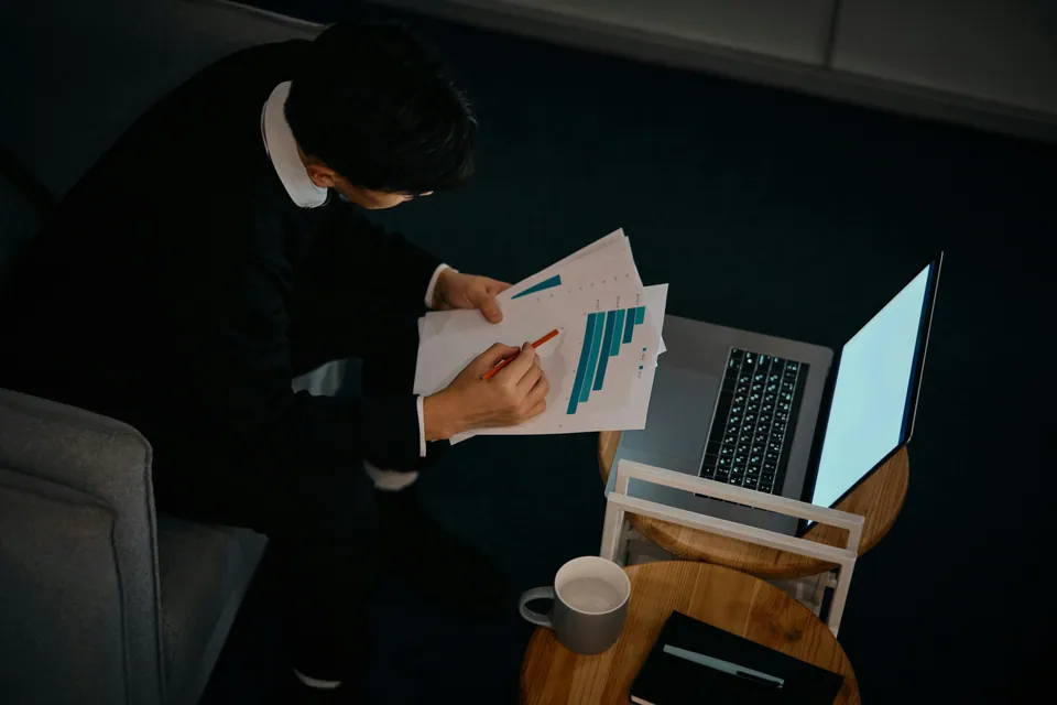 Person reviewing printed bar charts beside a laptop at a side table