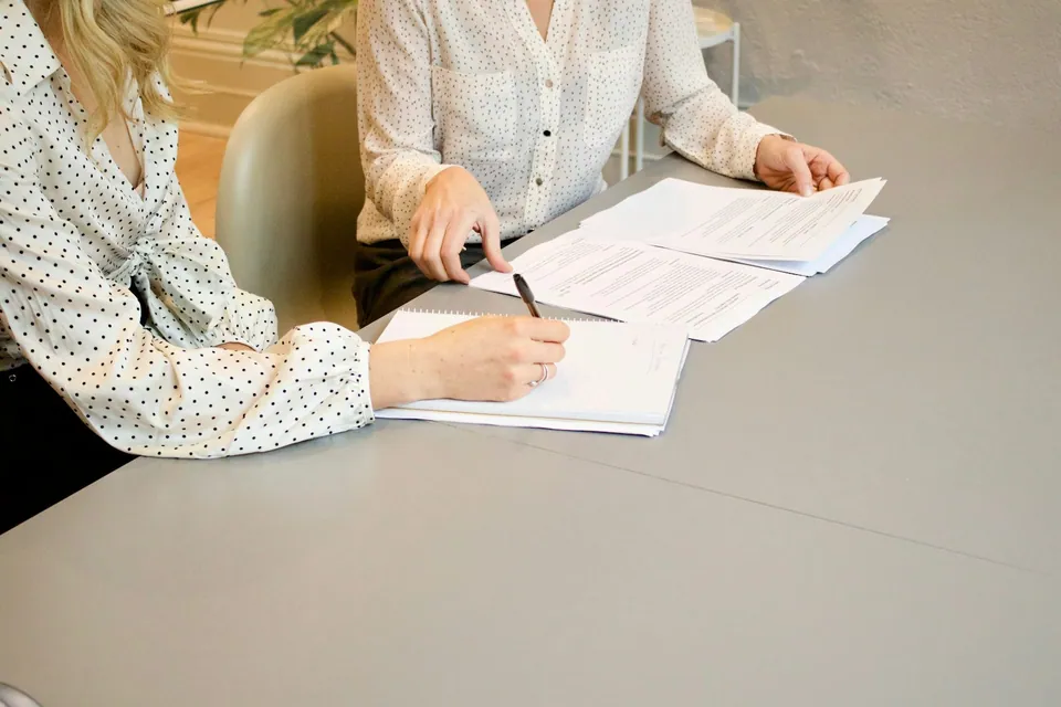 Two people signing paperwork at a gray table