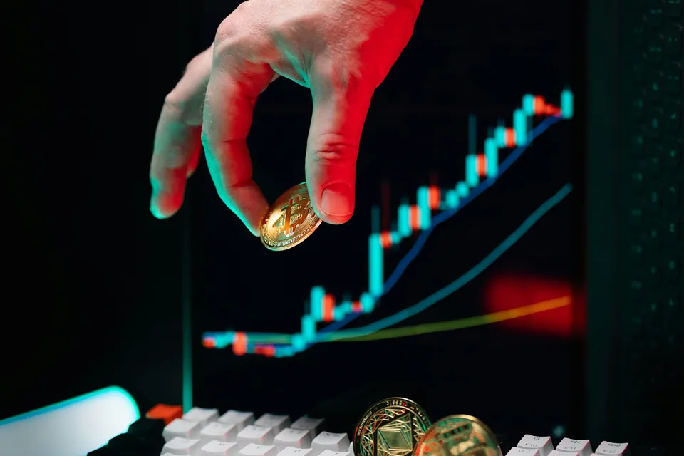 Hand holding a gold coin in front of a rising candlestick chart