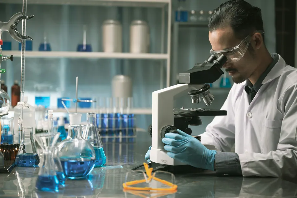 Scientist using a microscope in a lab with blue flasks