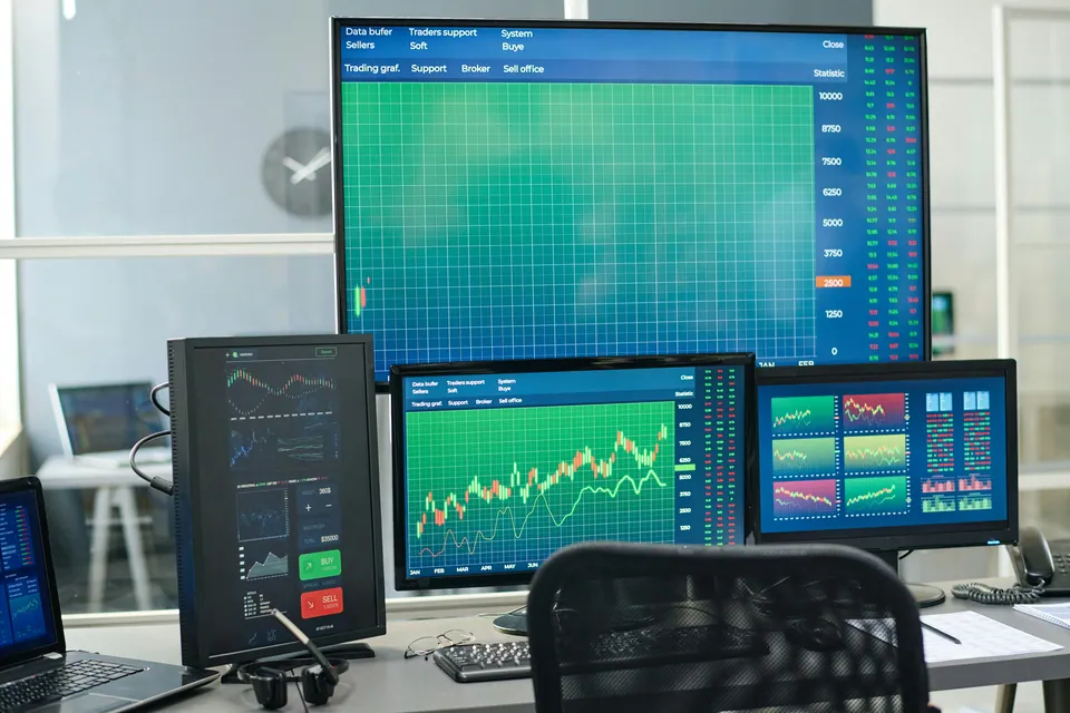 Trading desk with several monitors showing green charts