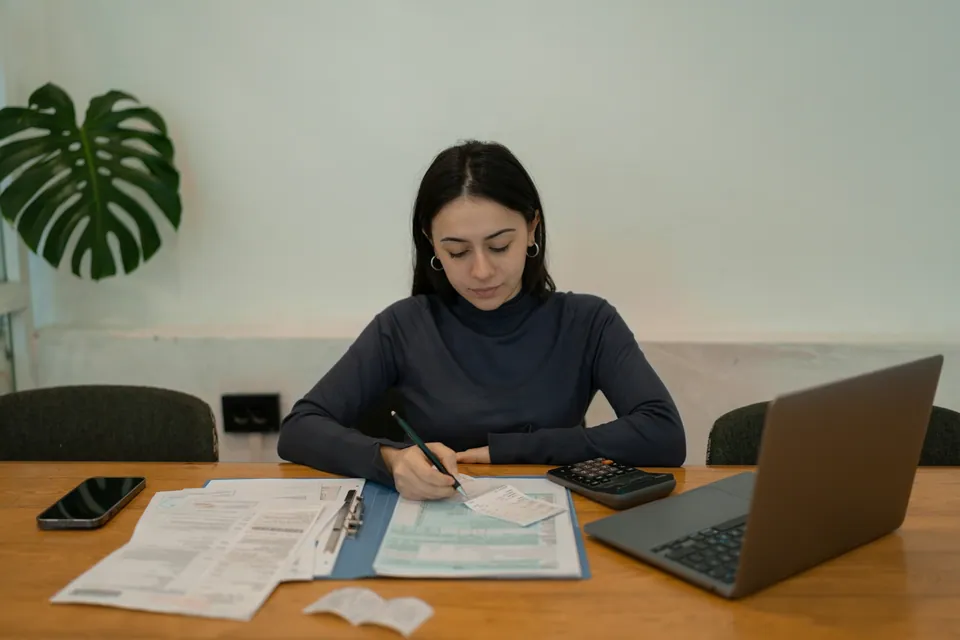 Woman working through paperwork beside a laptop and calculator