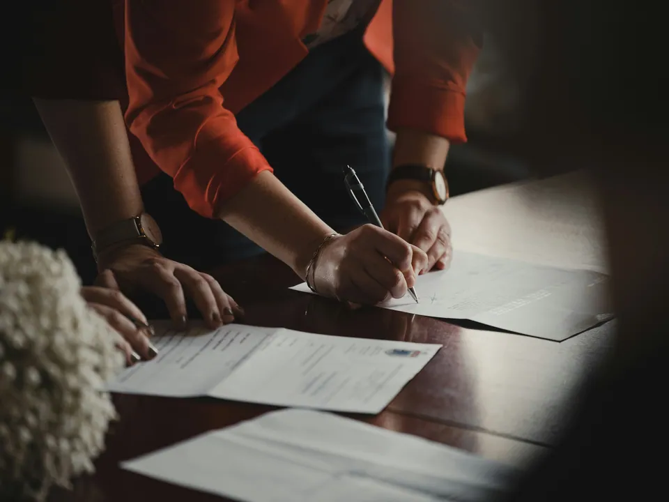 Hands signing documents on a dark wooden table