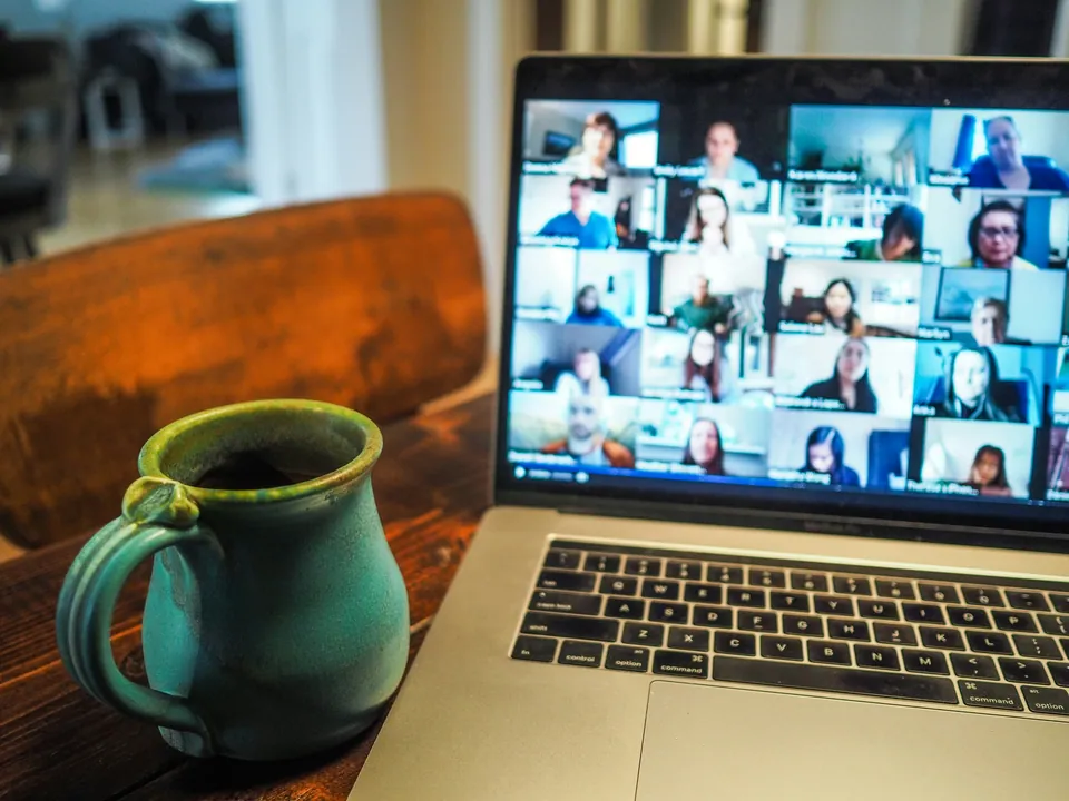 Laptop showing a video call grid beside a green mug