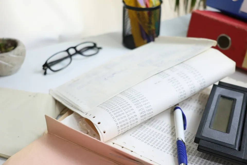 Glasses, an open ledger and a pen on a desk