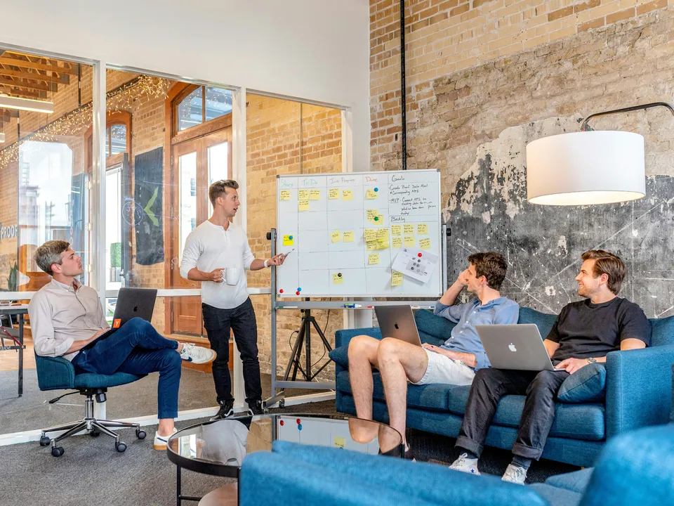 Small team meeting on sofas in a loft office with a whiteboard of sticky notes