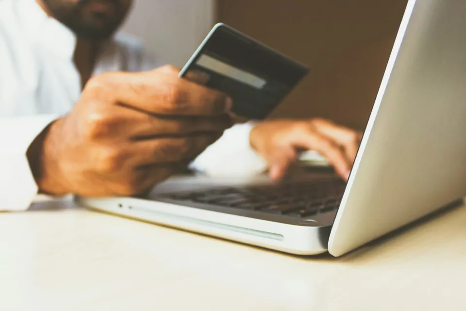 Hand holding a credit card while typing on a laptop